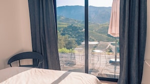 Quarto com uma cama grande, uma cadeira e vista para um vinhedo através de uma porta de vidro deslizante.