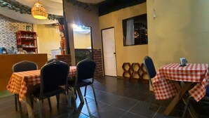 A restaurant interior with checkered tablecloths, metal chairs, a wicker hanging light fixture, and a brick wall. - Casa Florencia (Santa Ana)