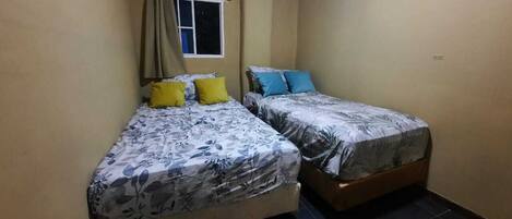 Quarto pequeno com duas camas de solteiro, cada uma com roupa de cama e almofadas estampadas com motivos florais em amarelo e azul.