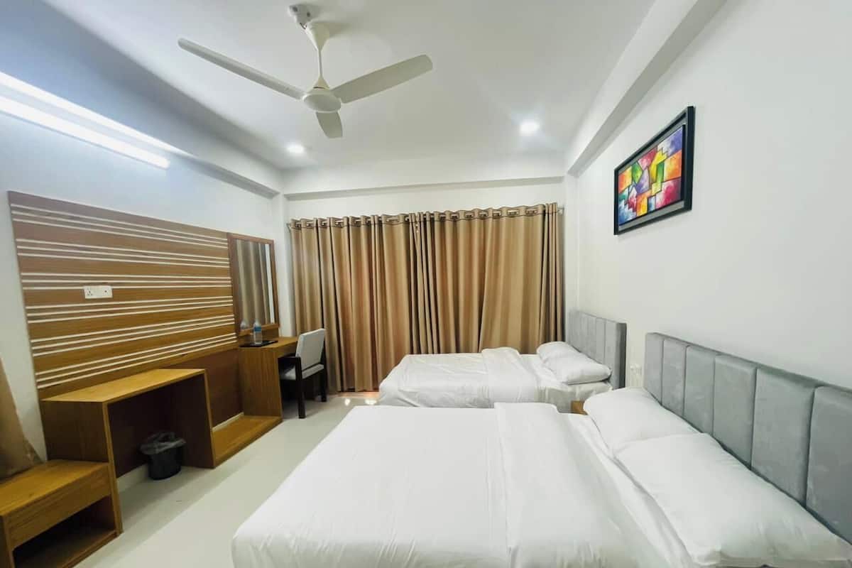 A hotel room with two beds, a desk, a chair, a ceiling fan, and a painting on the wall.
