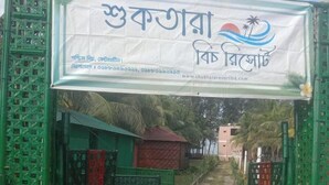 A gated entrance with a signboard, a pathway leading to a building, and a tropical setting with palm trees. - Shuktara Beach Resort Saint Martin (Saint Martin's Island)