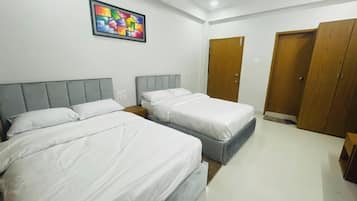Habitación de hotel con dos camas, un armario de madera, un cuadro abstracto de colores y un suelo de baldosas blancas.