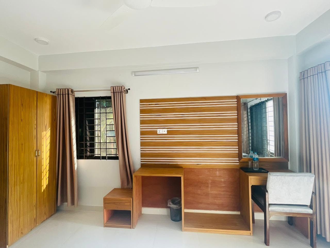 A bedroom with a wooden desk, a chair, a wardrobe, and a window with curtains.