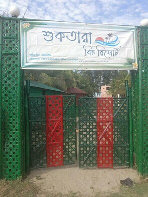 A gated entrance with a banner displaying text in a non-English script, likely indicating a hotel or resort. - Shuktara Beach Resort Saint Martin (Saint Martin's Island)