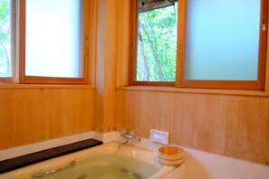 A wooden cabin bathroom with a bathtub, a window, and a view of trees.