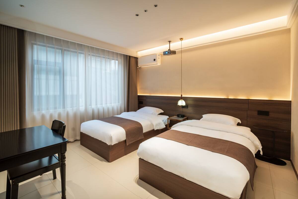 Una habitación de hotel con dos camas, un escritorio y un ventanal con cortinas.