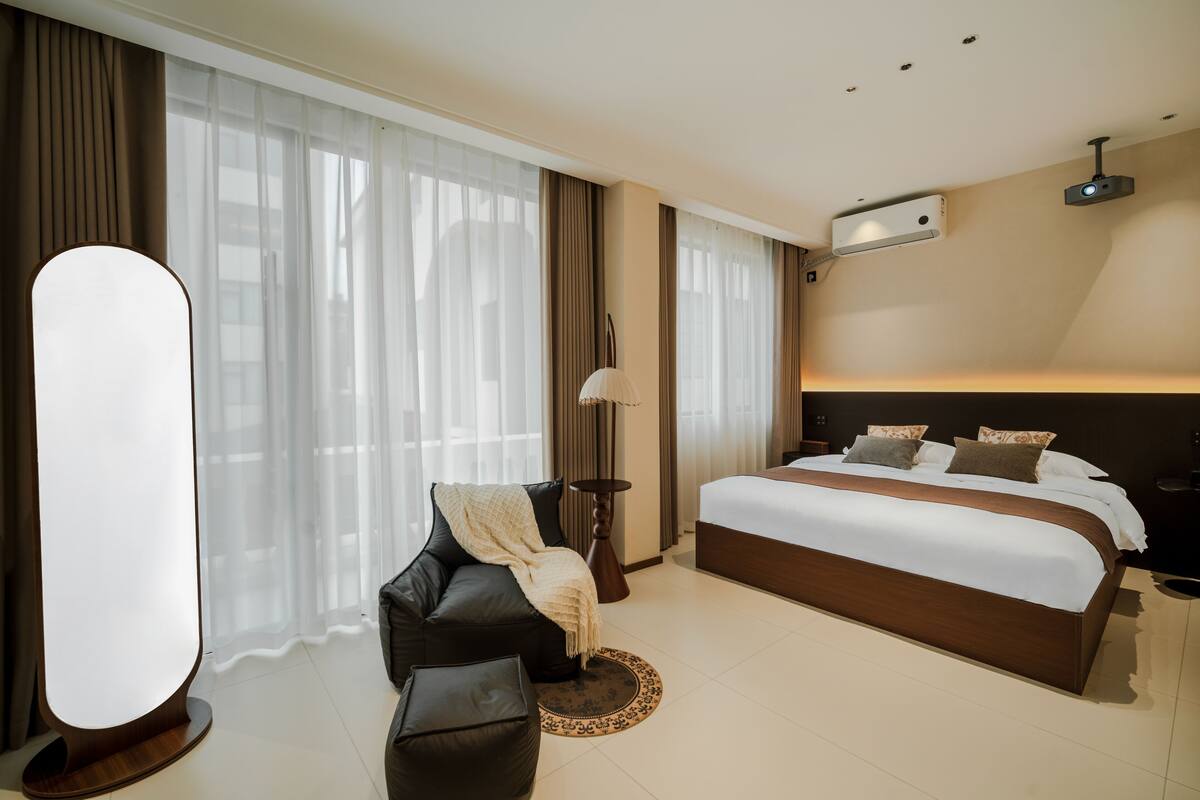 Una habitación de hotel moderna con una cama grande, un sofá, una mesita auxiliar y una lámpara de pie.
