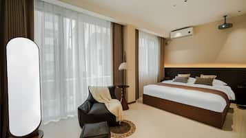 A modern hotel room with a large bed, a sofa, a side table, and a floor lamp.