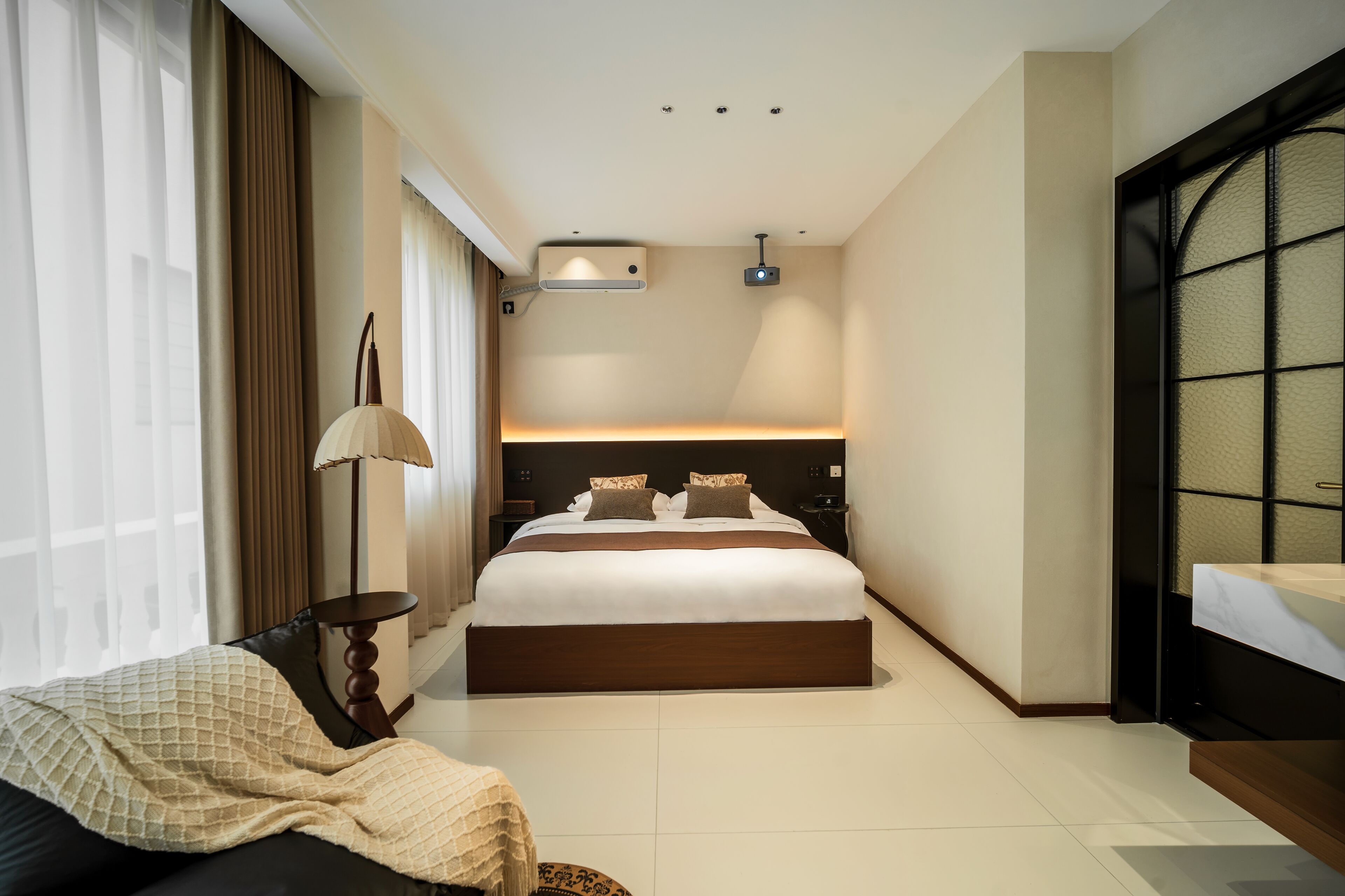 Un hotel moderno con una cama grande, una mesita de noche, una lámpara y vistas a la ciudad a través de una ventana.