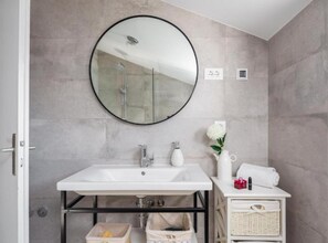 A bathroom with a round mirror, white sink, and a small white cabinet with toiletries. - Modern Villa With Pool Nancy (Sibenik)