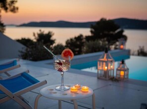 A sunset view from a poolside area with a drink, candles, and lounge chairs. - Modern Villa With Pool Nancy (Sibenik)