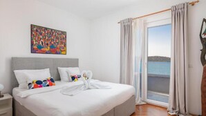 A bedroom with a large bed, a nightstand, a painting on the wall, and a view of the sea through a window. - Modern Villa With Pool Nancy (Sibenik)
