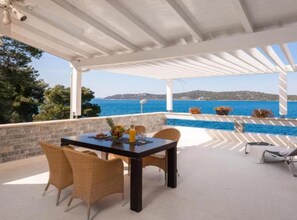A covered outdoor seating area with a table and chairs, overlooking a pool and the sea. - Modern Villa With Pool Nancy (Sibenik)