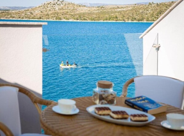 Varanda com mesa posta para o café da manhã, com vista para um mar azul e límpido.