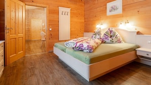 A wooden cabin bedroom with a bed, bedside tables, and a door leading to another room. - Holiday Home in Salzburg with Alpine View (Leogang)