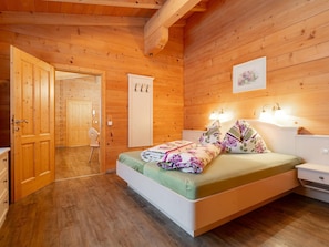 A wooden cabin bedroom with a bed, bedside tables, and a door leading to another room. - Holiday Home in Salzburg with Alpine View (Leogang)