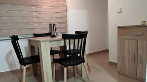 A small dining area with a wooden table and four black chairs. There is a cabinet to the right and a window with blinds in the background. - Apartments Adriana (Gradac)