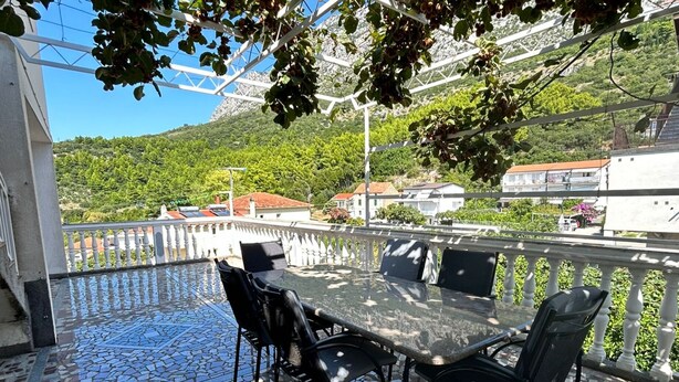 A terrace with a mosaic floor, outdoor seating, and a view of a hillside with buildings. - Apartments Adriana (Gradac)