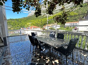 A terrace with a mosaic floor, outdoor seating, and a view of a hillside with buildings. - Apartments Adriana (Gradac)