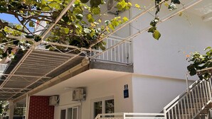 A multi-story building with a white exterior, a red brick wall, and a balcony with a metal railing. - Apartments Adriana (Gradac)