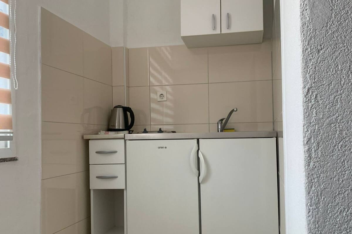 A compact kitchen with a built-in refrigerator, a kettle, and a sink.