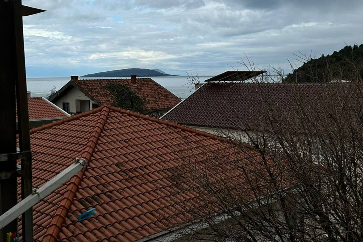 A residential area with terracotta-tiled roofs, a body of water, and a distant mountain.