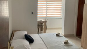 A hotel room with a bed, a small table with a cup and a towel, a window with blinds, and a door. - Apartments Adriana (Gradac)