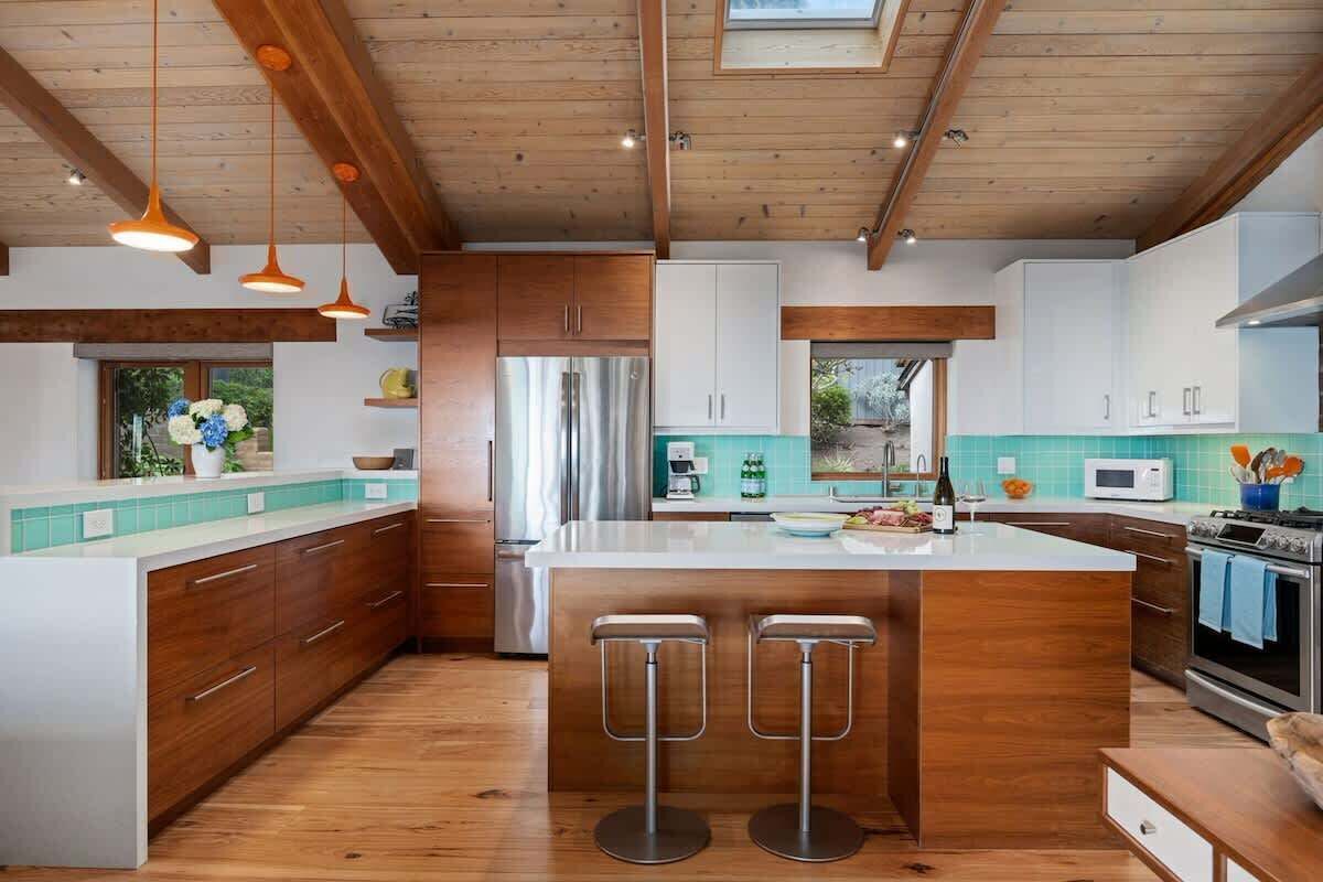 Una cucina moderna con mobili in legno, un'isola centrale con sgabelli da bar, elettrodomestici in acciaio inossidabile e un lucernario.