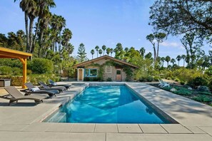 A swimming pool with lounge chairs, a small building, and surrounding palm trees.