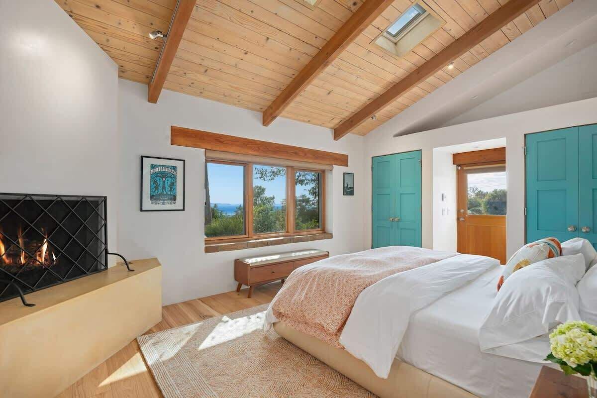 A bedroom with a fireplace, a large bed, a window with a view, and a door.
