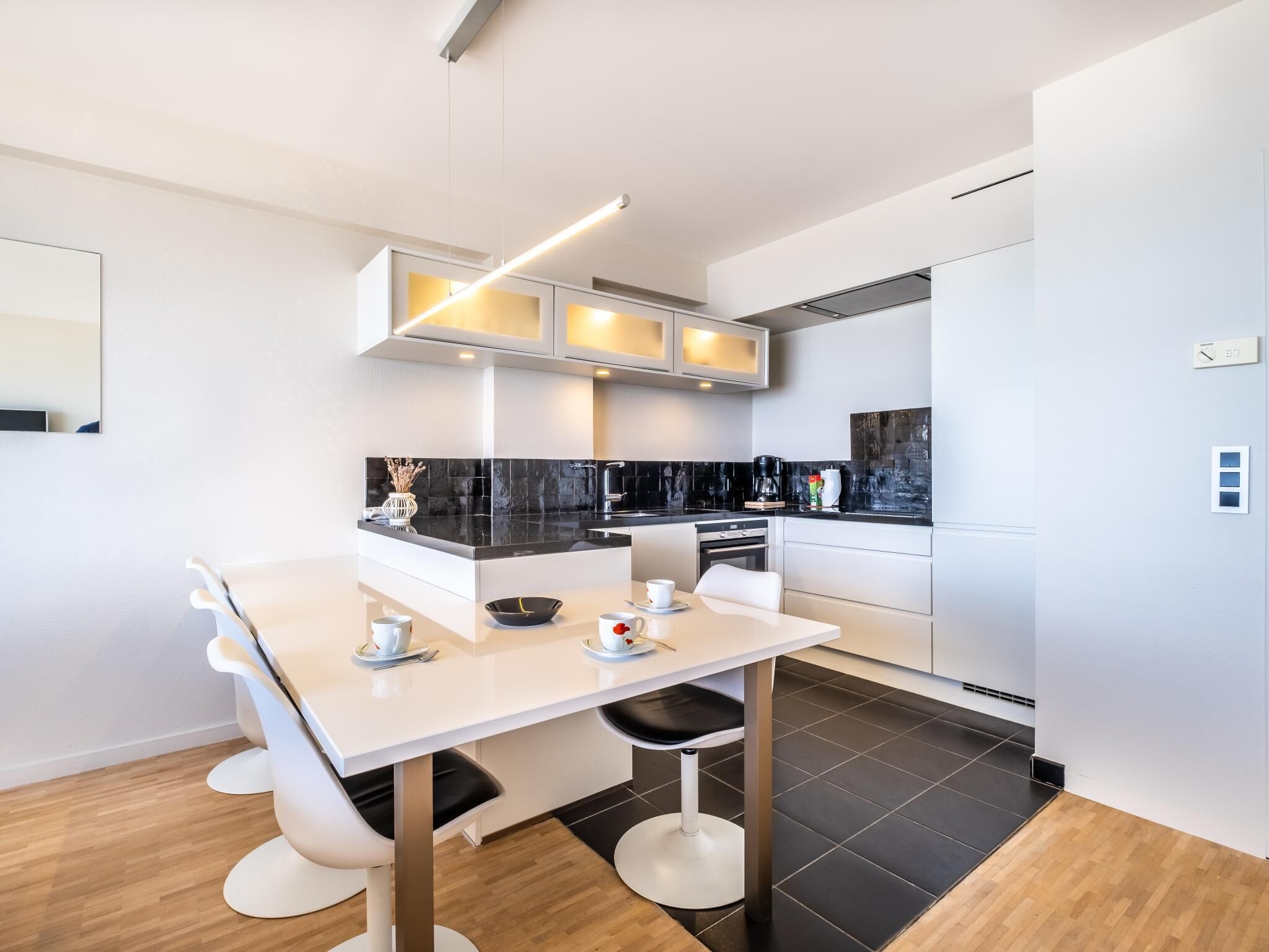 Una cocina moderna con muebles blancos, encimeras negras y un comedor con mesa y sillas blancas.