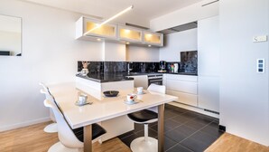 Una cocina moderna con muebles blancos, encimeras negras y un comedor con mesa y sillas blancas.