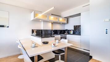 Una cocina moderna con muebles blancos, encimeras negras y un comedor con mesa y sillas blancas.