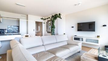Una sala de estar moderna con un sofá blanco, un televisor y una cocina al fondo.