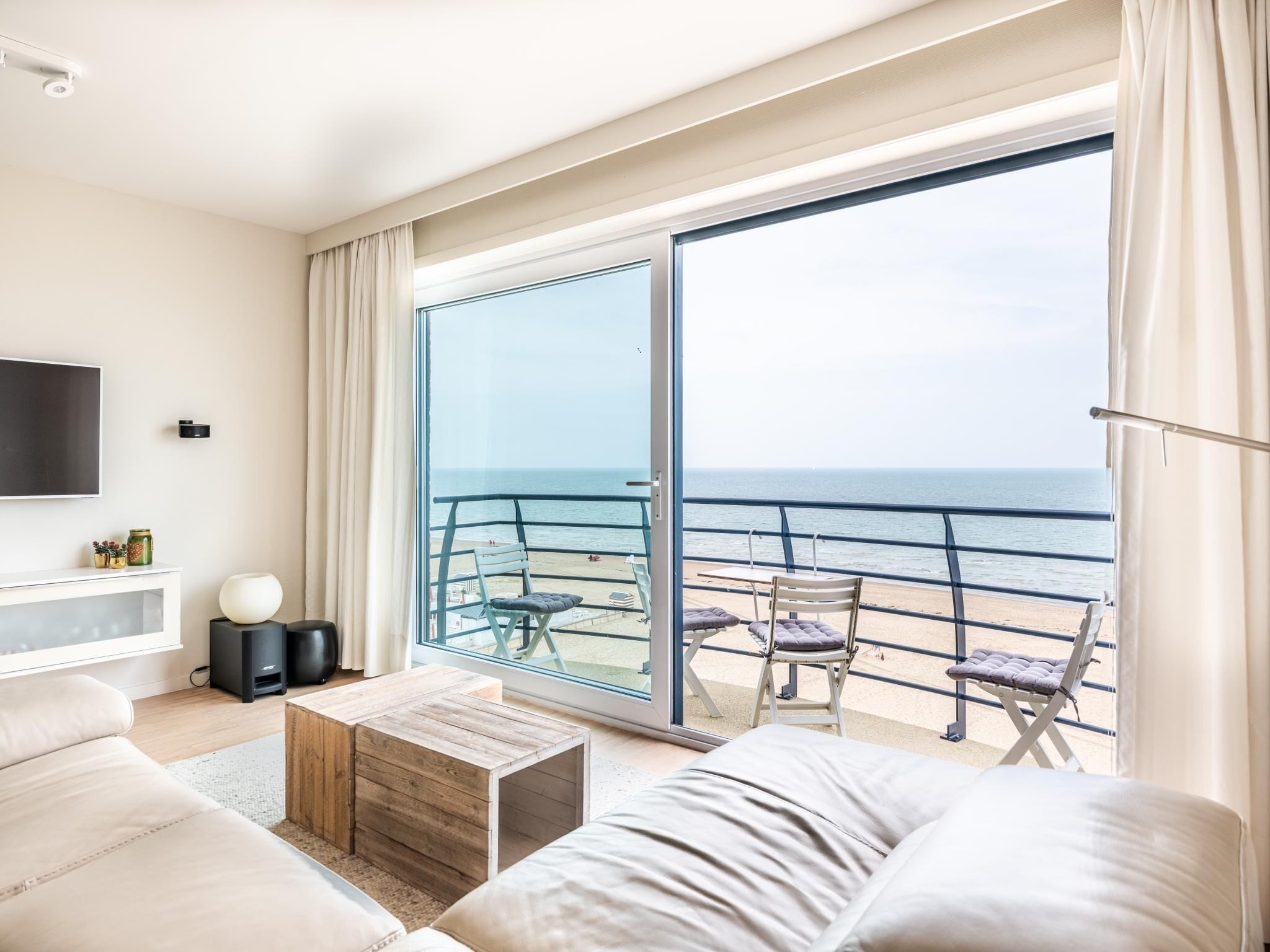 Un salón moderno con un amplio ventanal corredero que da a un balcón con vistas al mar.