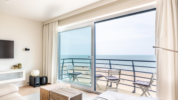 Un salón moderno con un amplio ventanal corredero que da a un balcón con vistas al mar.