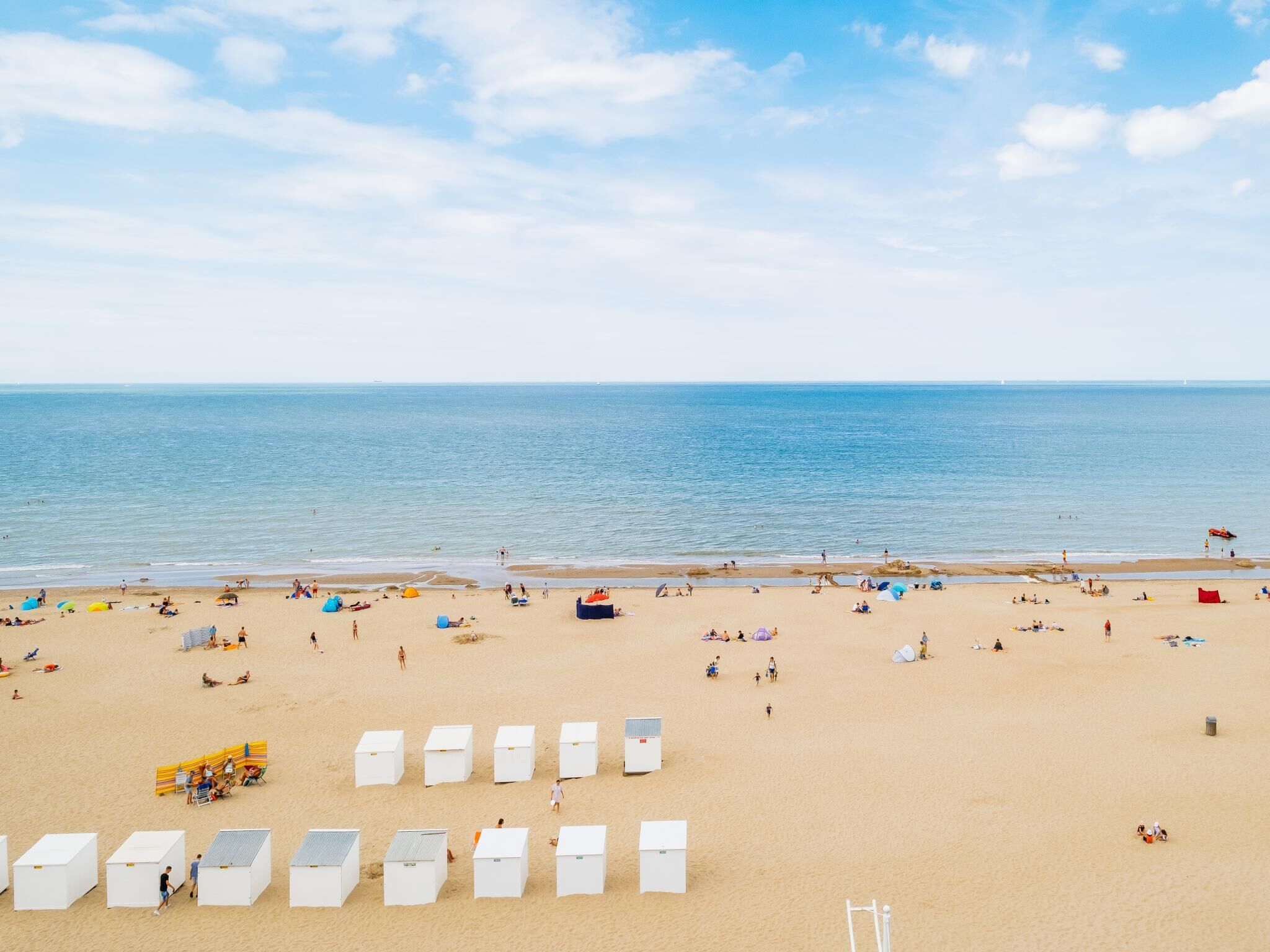 Una playa con cabañas blancas y gente relajándose.