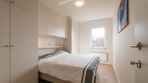A bedroom with a bed, a window, and a painting on the wall. - Cosy flat with beautiful terrace (Koksijde)