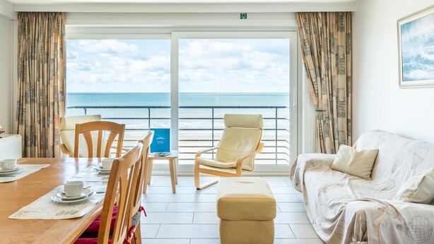 A room with a dining table, chairs, a sofa, and a view of the sea through large windows. - Wake up to sea views (Koksijde)