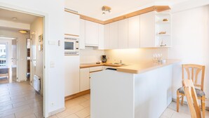 A modern kitchen with white cabinetry, a central island, and a built-in microwave. - Wake up to sea views (Koksijde)