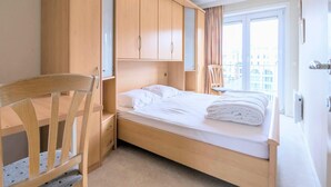 A bedroom with a bed, wooden wardrobe, desk, chair, and a window with curtains. - Wake up to sea views (Koksijde)