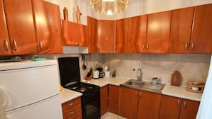 A kitchen with wooden cabinets, a white refrigerator, a black stove, and a sink. - Apartman Olive Garden (Solta)