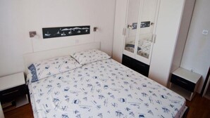 A bedroom with a bed, a wardrobe, a nightstand, and a wall-mounted shelf with a picture. - Apartman Olive Garden (Solta)
