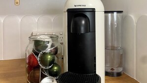 A kitchen counter with a Nespresso coffee machine, a jar of coffee beans, a mug, and a container of biscotti.