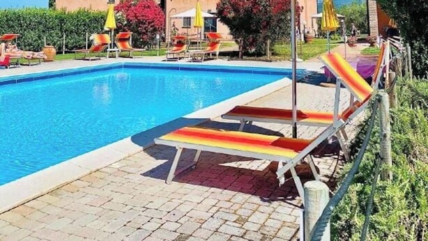 A swimming pool with lounge chairs and umbrellas, surrounded by a building with a tiled roof. - 4sleeping places with swimming pool, parking space (Campiglia Marittima)