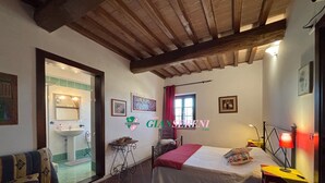 A bedroom with a bed, a bedside table, a chair, a window with curtains, and a bathroom with a sink and mirror. - 4sleeping places with swimming pool, parking space (Campiglia Marittima)