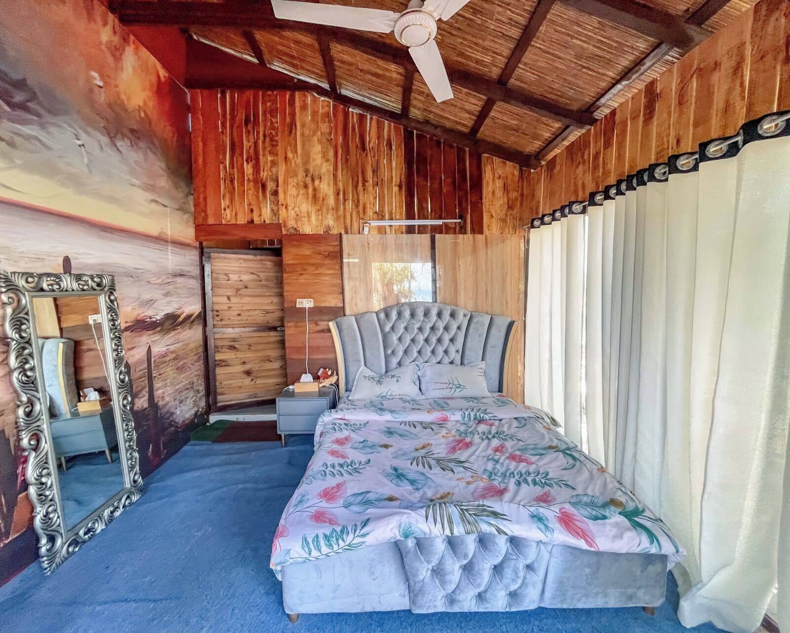 A bedroom with a bed, a mirror, a ceiling fan, and wooden walls.