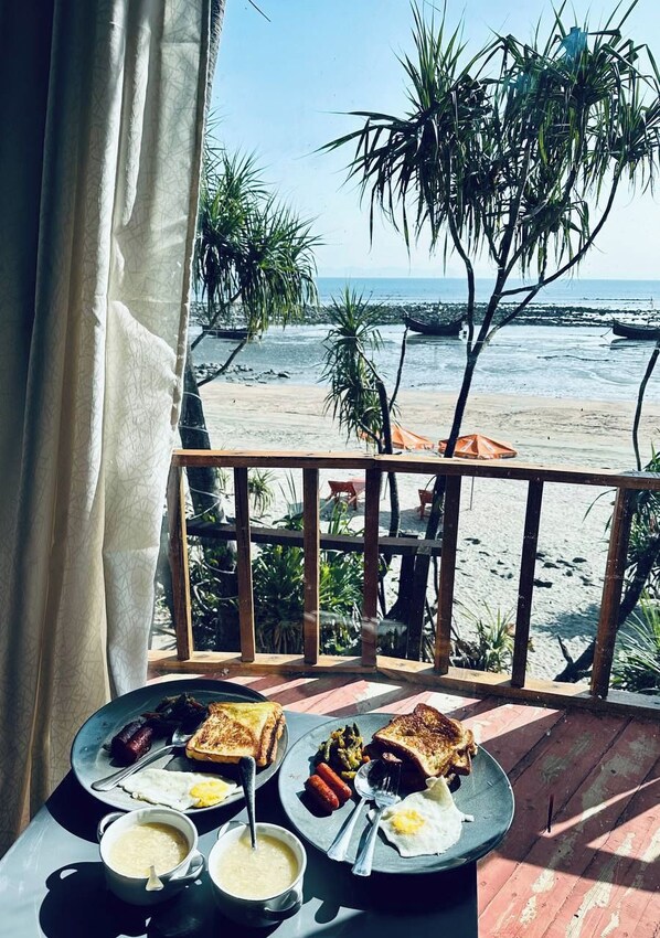 A balcony with a table set for breakfast overlooking a beach. - Nongoor Eco Beach Resort Saint Martin (Saint Martin's Island)