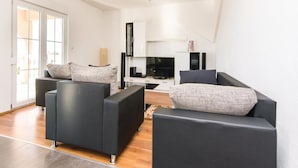 A modern living room with black sofas, a flat-screen TV, and a large window. - Amazing Villa With Outdoor Swimming Pool (Stankovci)