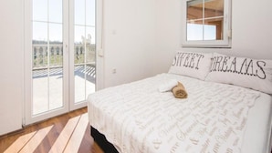 A bedroom with a large sliding glass door leading to a balcony, a bed with a white duvet and pillows, and a window above the bed. - Amazing Villa With Outdoor Swimming Pool (Stankovci)